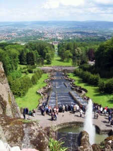 View from the Bergpark Wilhelmshöhe (mountain park) to Kassel, with the Baroque Water feature in operation. In background the castle Wilhelmshöhe and street "Wilhelmshöher Allee" to city. Wikimedia Commons.